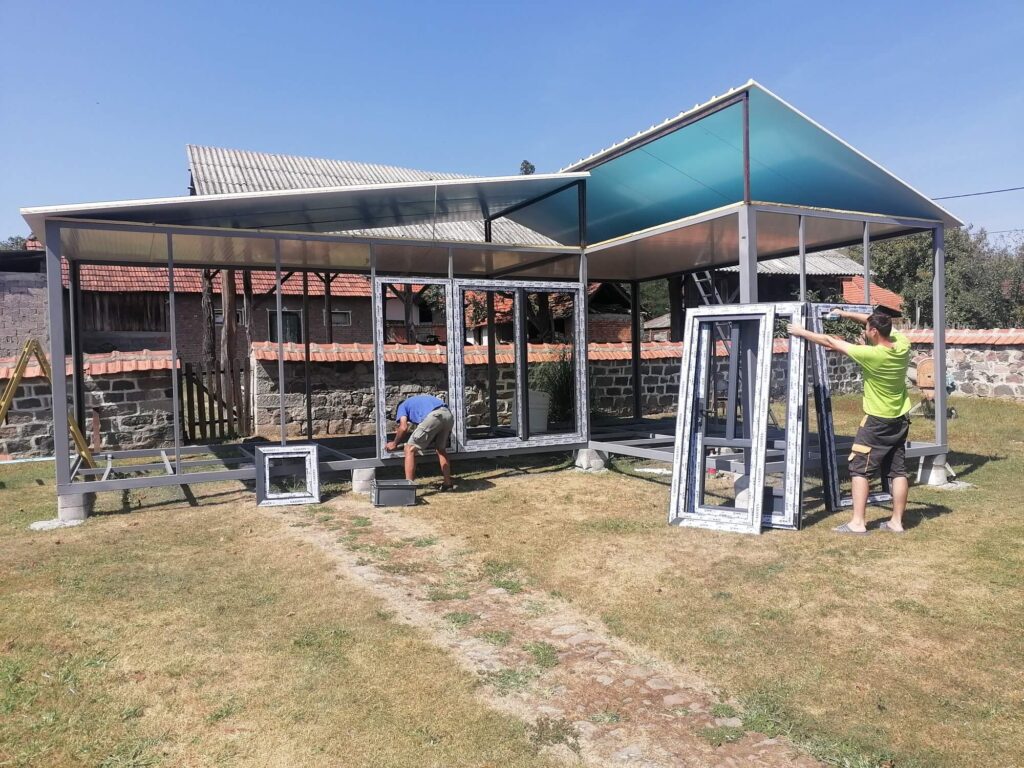 Dva radnika postavljaju prozore i konstrukciju za modularnu kućicu na selu