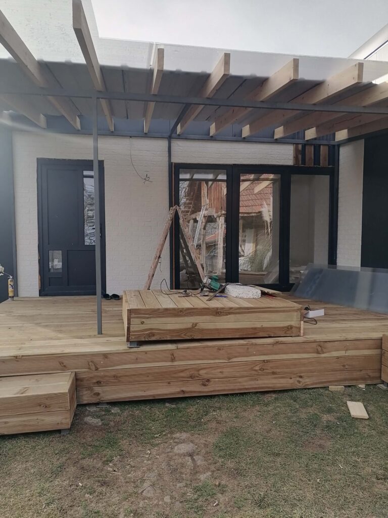 Drvena terasa i pergola u izgradnji ispred modularne
 kućice sa tamnim vratima i prozorima